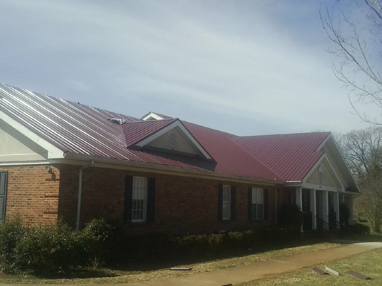 Red metal roof with gabled entries on a long brick building, from a Hail Damage Roof Repair job in Oakwood