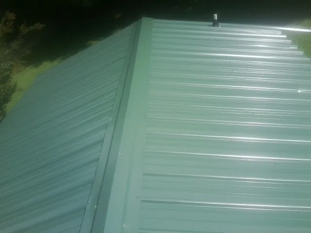 New green metal panels meeting at the ridge of a roof — Flat Roof Repair work by our crew in Oakwood