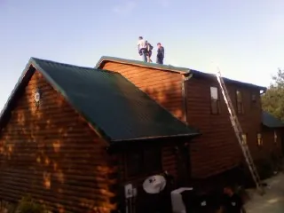 Crew on the ridge of a green metal roof on a two story log home in Oakwood